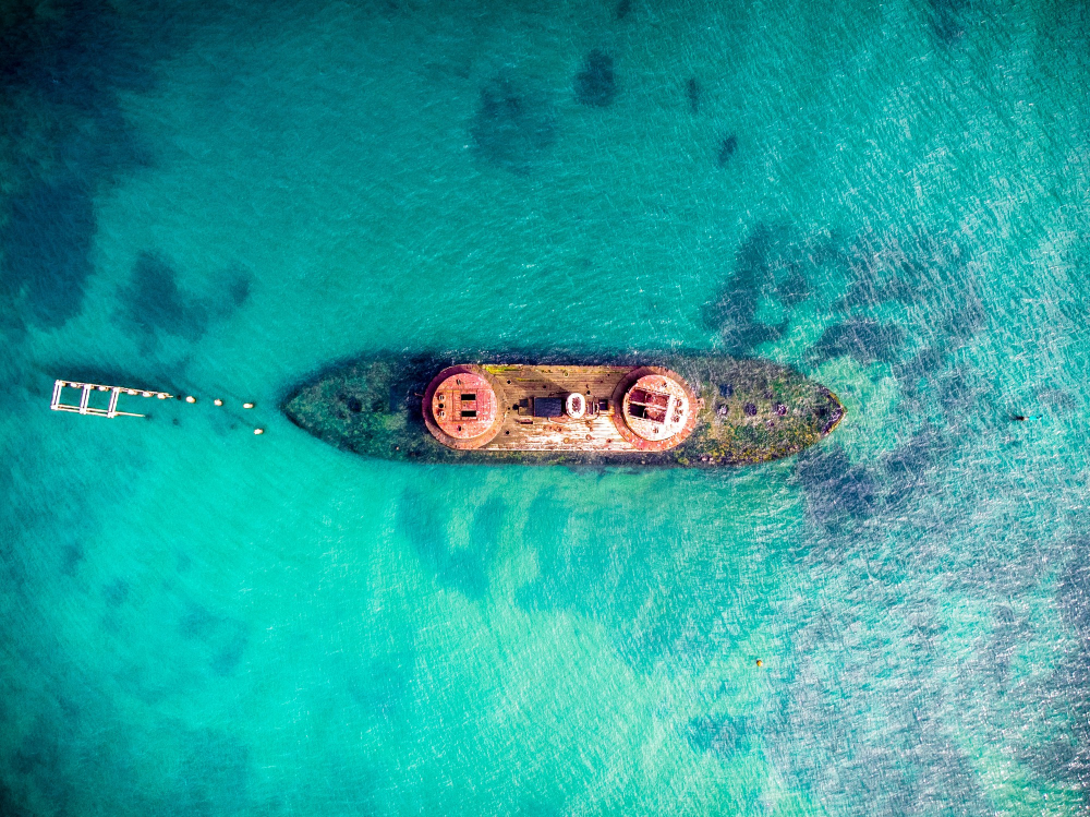 Aerial view of Naked Island sandbar, Siargao, white mound surrounded by gradients of turquoise and blue water, outrigger banca boat in frame