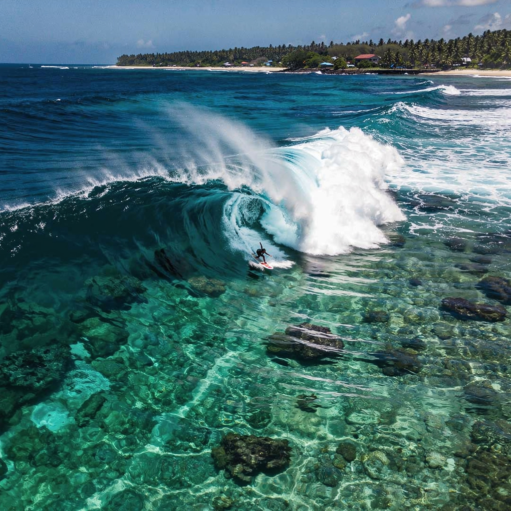 Aerial view of Cloud 9 surf break in Siargao, Philippines, with a surfer dropping into a hollow right-hand barrel over shallow turquoise reef water